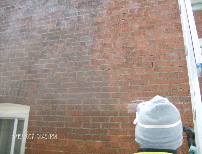 Mason in a hat and vest working on a red brick wall beside a window