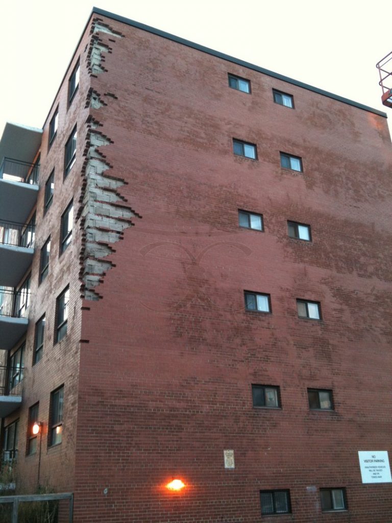 Corner of a six-storey red brick apartment building with broken, stepped brick along the edge