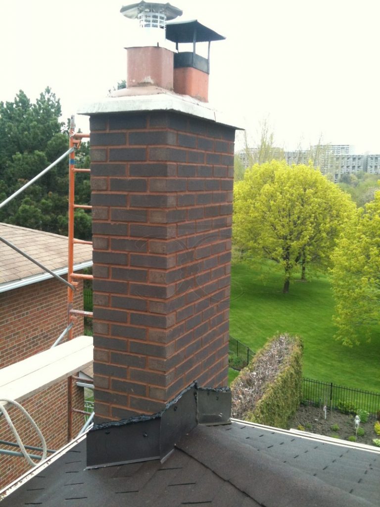 Rebuilt brick chimney stack above a roofline, with scaffolding still beside it