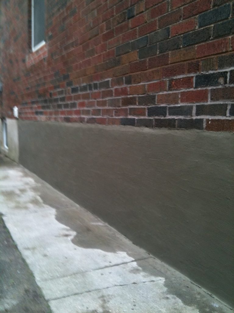 New grey parging along a foundation wall below red brick