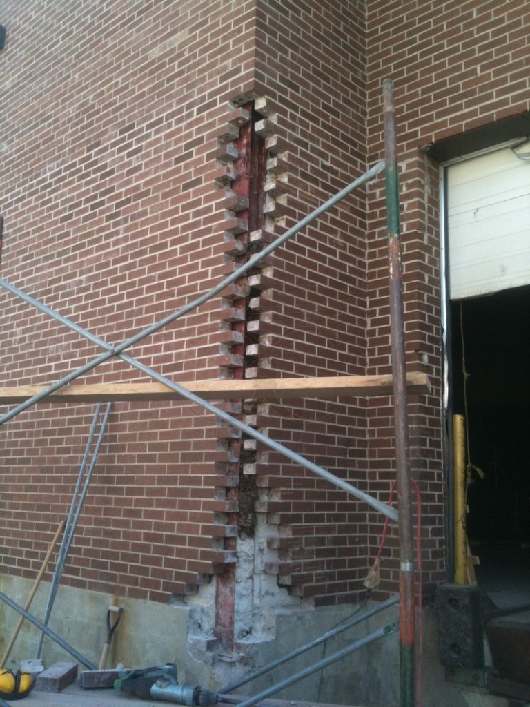 Commercial brick wall with scaffolding and a column of exposed bricks beside a door