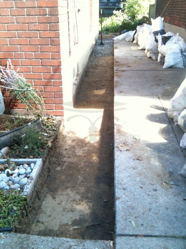 Excavated strip along a building wall with bags of rubble nearby
