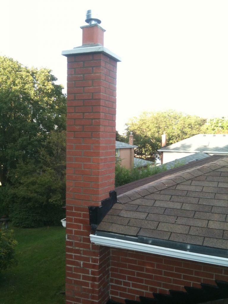 Brick chimney rising above a shingled roof beside a house
