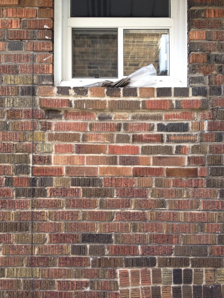 Brick wall below a window with broken and mismatched bricks
