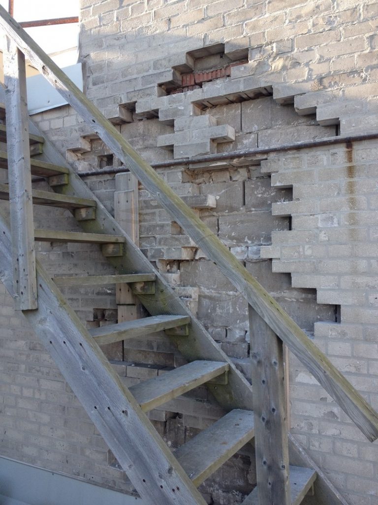 Brick wall behind an exterior staircase with a stepped section of bricks removed