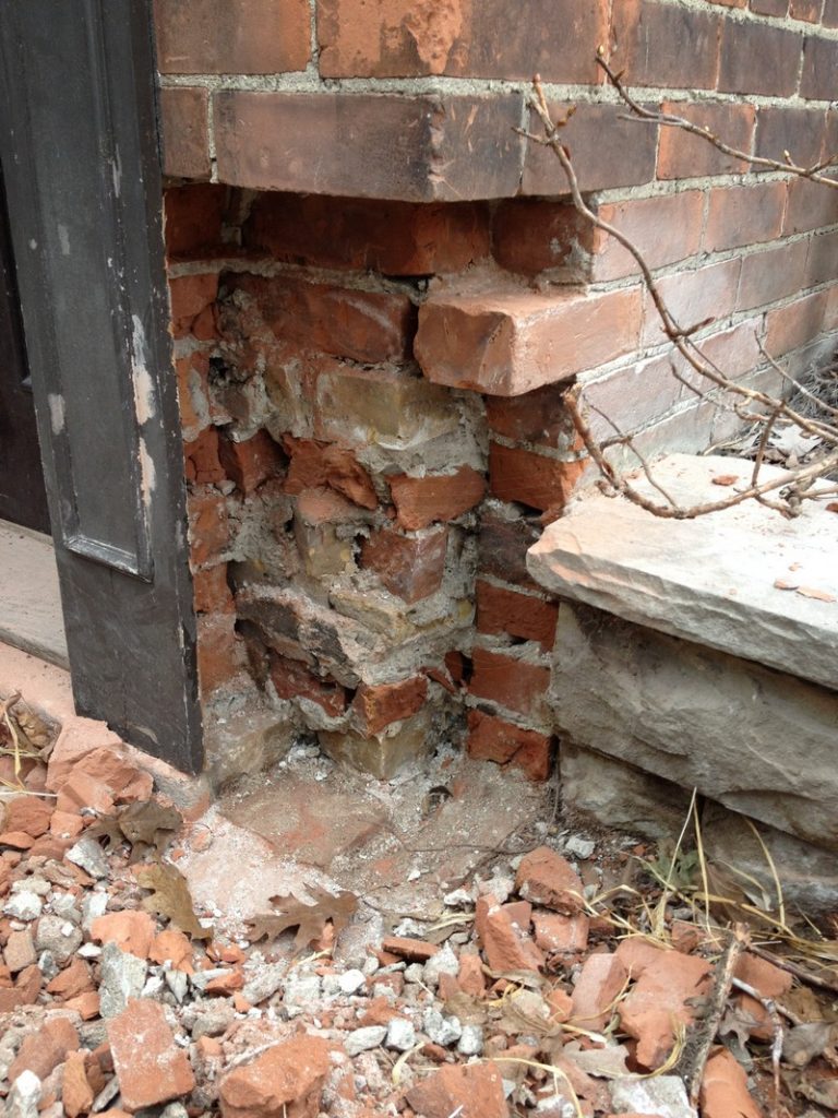 Broken brick and rubble at a doorway corner beside a stone step