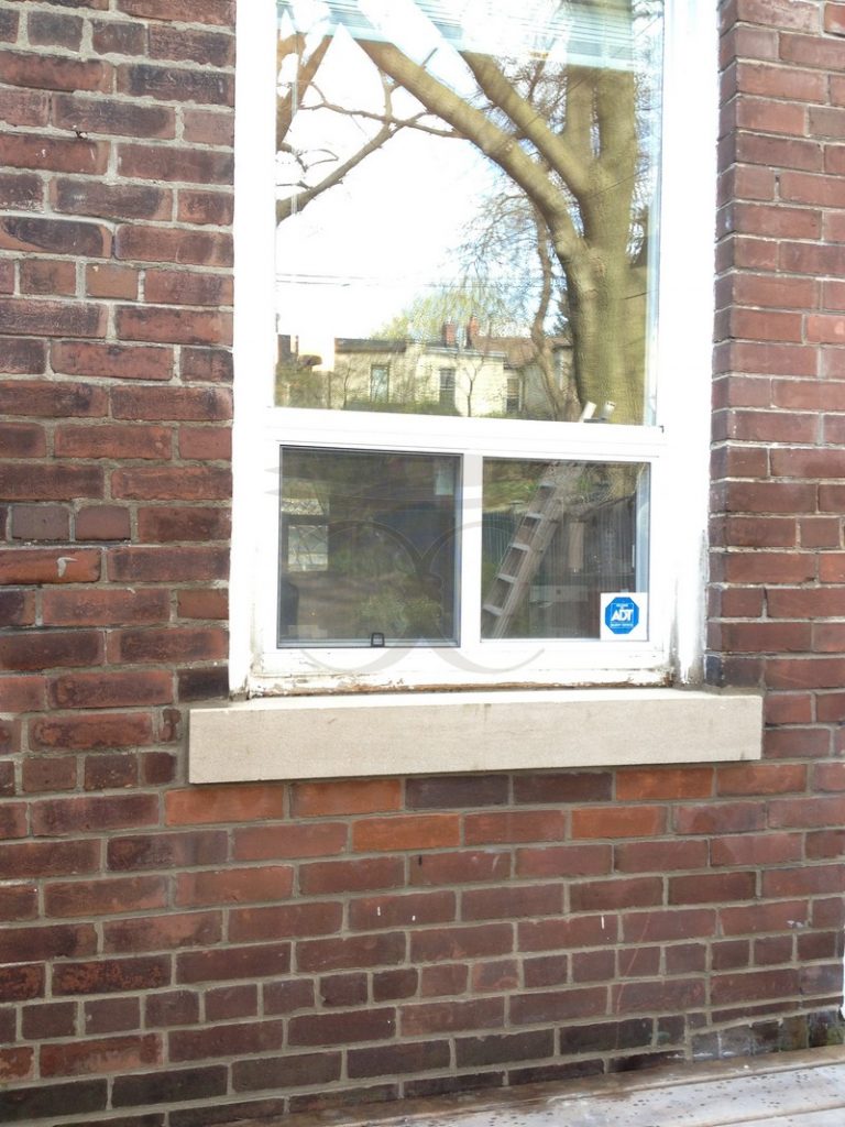 Red brick wall below a window after damaged bricks were cut out and replaced, with a new stone sill
