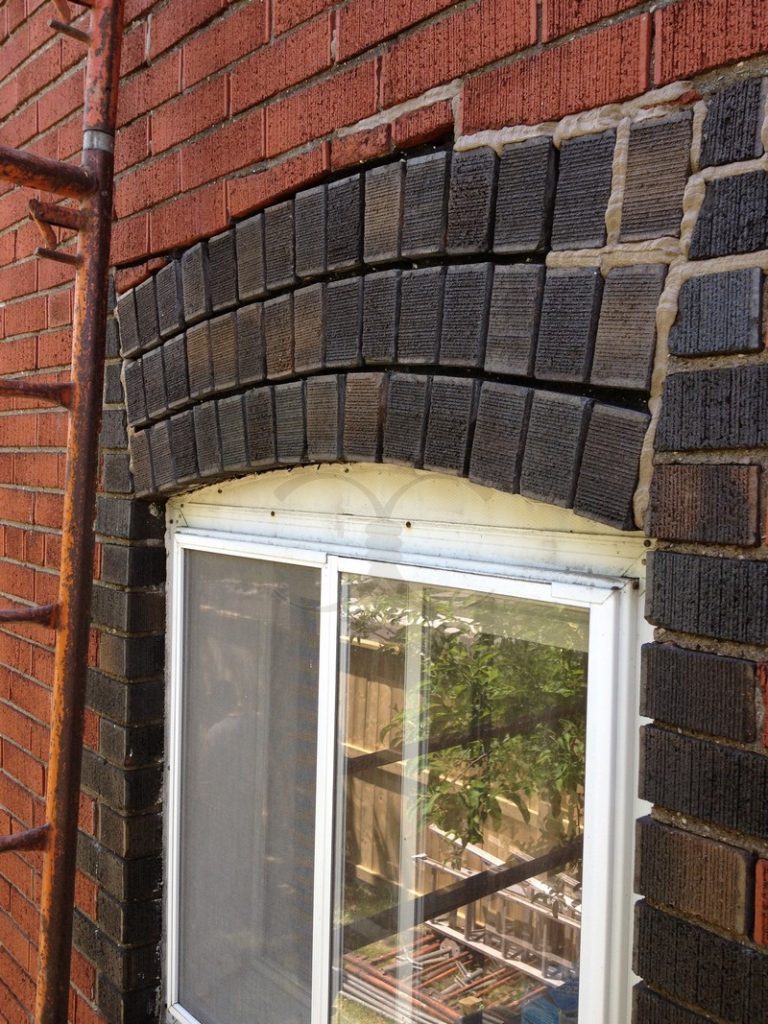 Dark brick arch above a basement window in a red brick wall