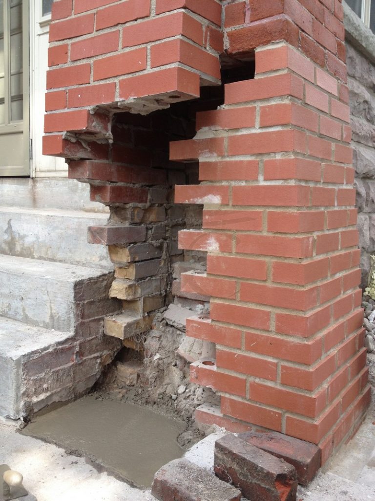 Brick pillar beside concrete steps with missing and broken brick