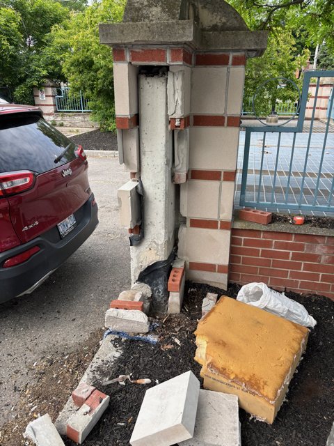 Damaged brick and stone gate pillar partly taken down, with broken bricks and stone caps on the ground