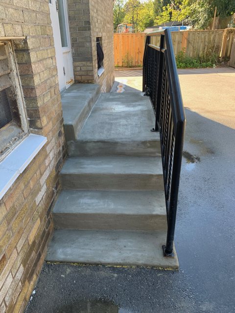 New concrete side-entry steps with a black metal railing beside a brick house
