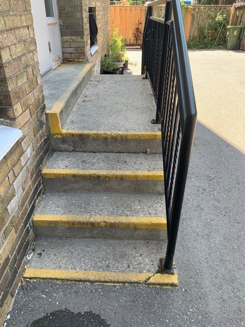 Worn concrete side-entry steps with painted yellow edges and a black railing