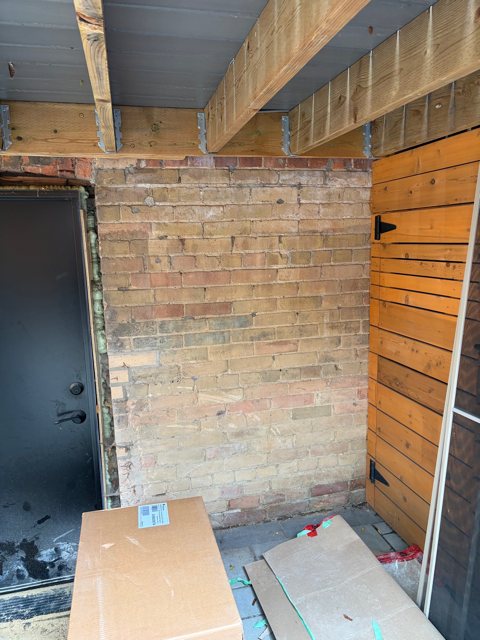 Buff brick wall under a wooden deck with an old door opening, during repair