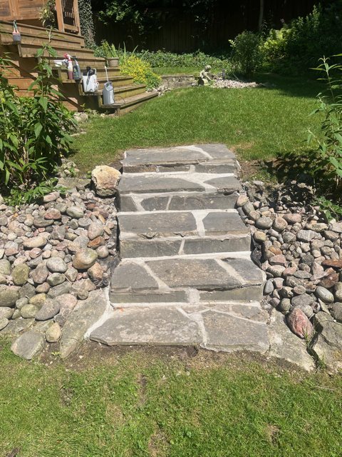 Rebuilt flagstone steps climbing a garden slope between river-rock borders
