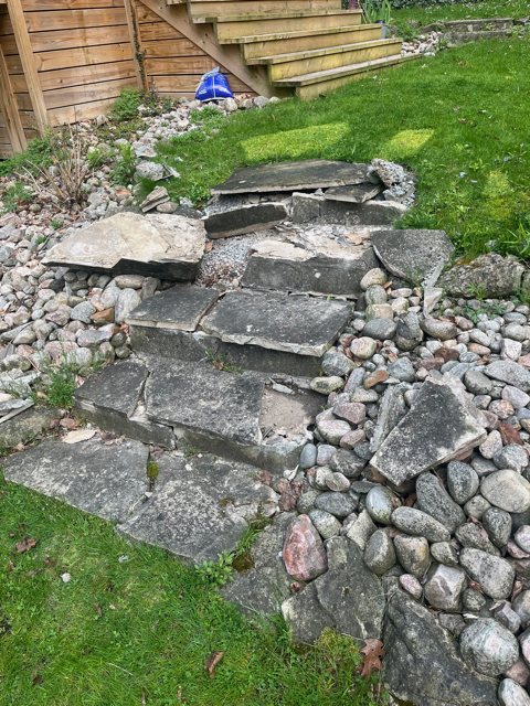 Loose, broken flagstone steps on a garden slope surrounded by river rock