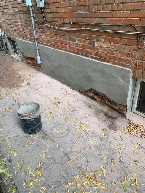 Cracked and peeling parging on a foundation wall below red brick
