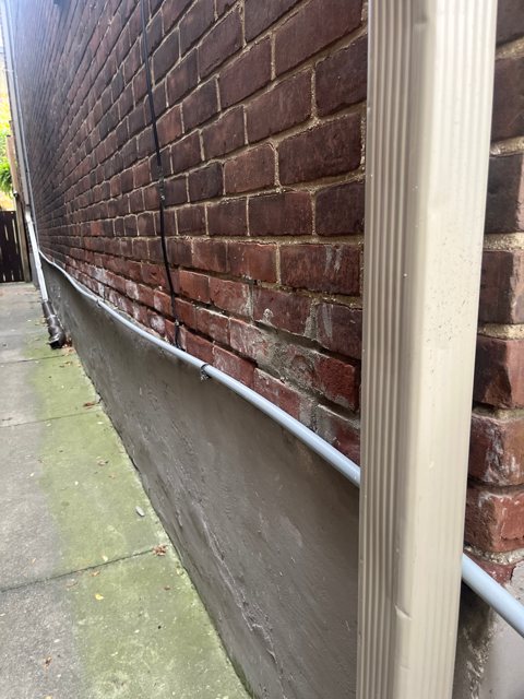 New grey parging on the foundation below a red brick wall beside a walkway