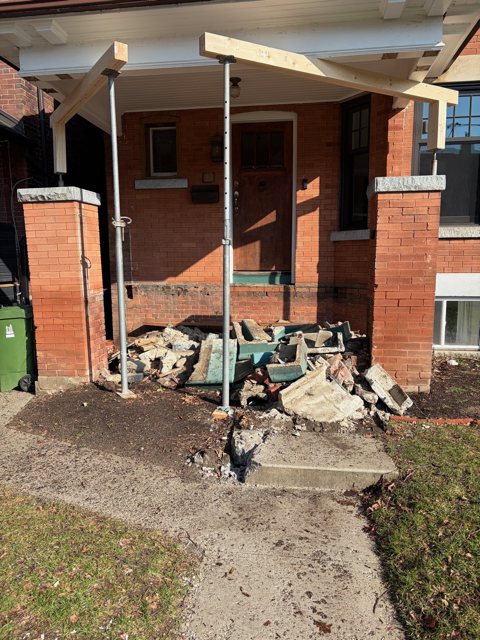 Porch roof held on temporary posts after the old brick pillars were taken down, with rubble on the walkway
