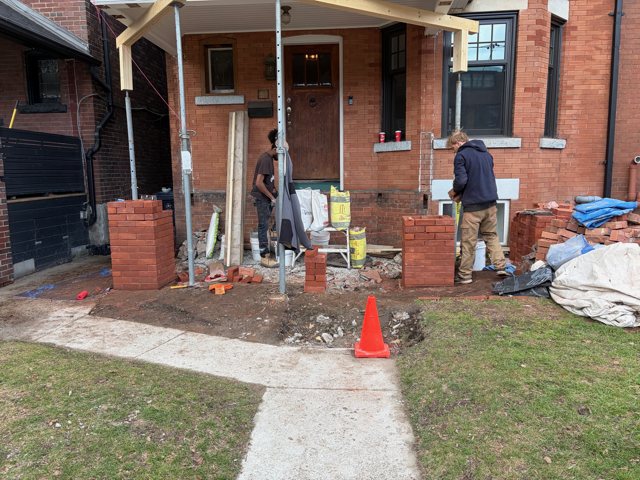 Masons rebuilding red brick porch pillars on a Toronto house, with the roof on temporary supports