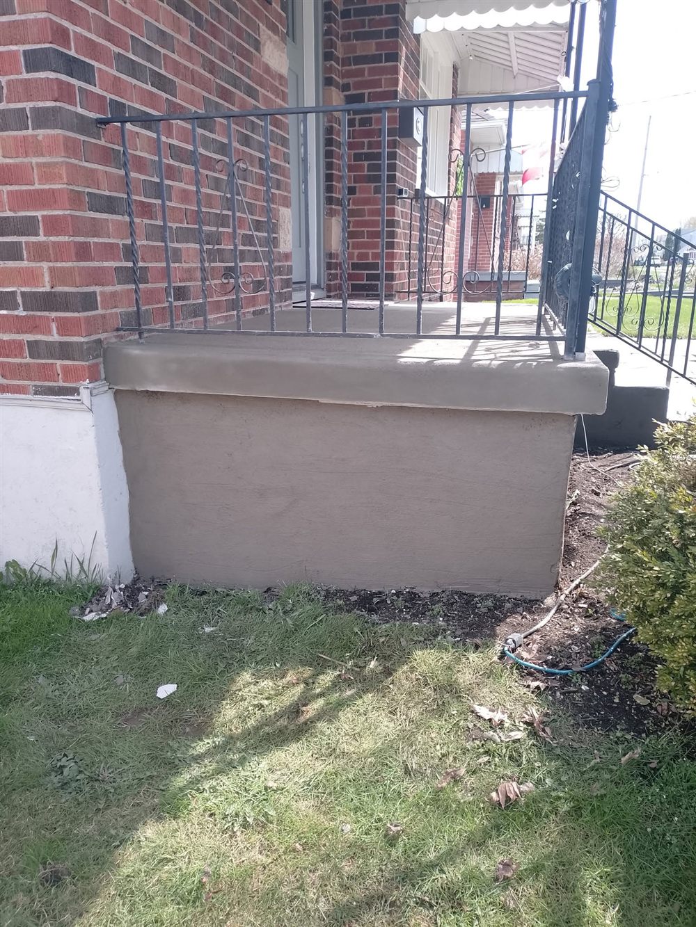 Front porch step wall finished with fresh grey parging beside a red brick house and iron railing