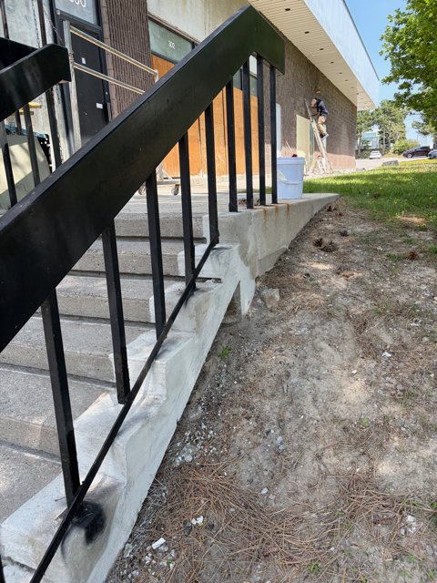 Repaired concrete side wall along the same exterior steps, clean and smooth beside a black metal railing